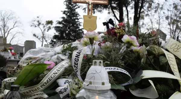 Wieniec pogrzebowy z krzyżem i płonącą świecą na cmentarzu.